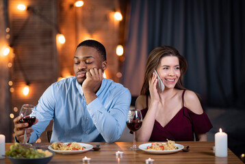 Black guy sitting bored while his girlfriend talking on cellphone in restaurant