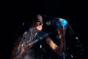 Side view of female sitting with Earth globe under plastic sheet demonstrating concept of environmental pollution