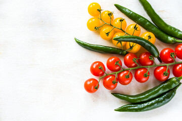 Green chilli peppers and colorful cherry tomatoes on the white background
