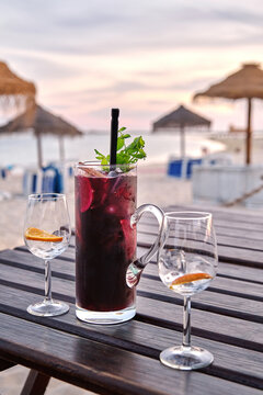 Tasty red cocktail with orange slices placed on wooden table with glass goblets on Fuseta Beach at sunset in summer