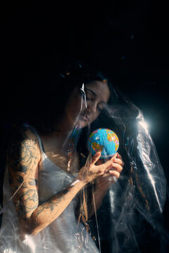 Side view of female sitting with Earth globe under plastic sheet demonstrating concept of environmental pollution