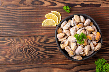 Frozen peeled mussels with parsley and lemon slices on wooden table, top view