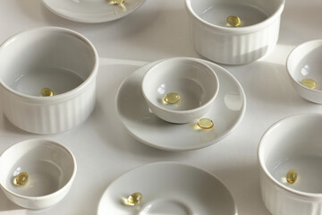 Fish oil pills supplement in whate plates and dishes on white table, monochrome abstract composition and design, modern art concept