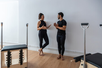 Cheerful sportsman and sportswoman standing in bright gym and talking to each other while relaxing during pilates training
