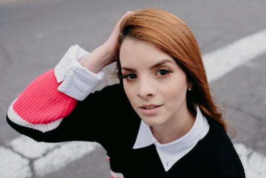 High angle of carefree female with red hair and in casual outfit standing in city street and looking at camera