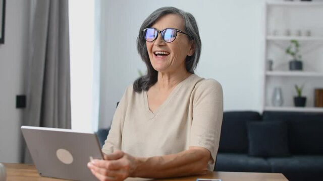 Cheerful confident senior woman using a digital tablet for video connection, remote meeting, smiling mature lady waving hello into webcam, greeting online interlocutors