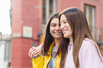 Content lesbian women waking along street and looking at each other while enjoying stroll on sunny day in city