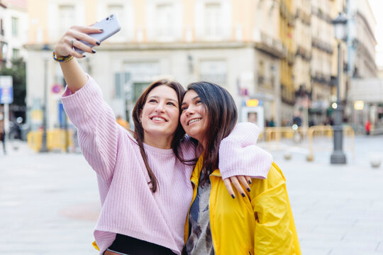 Smiling lesbian females embracing in city and taking self portrait on smartphone while spending time together at weekend