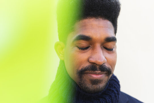 Through yellow light filter of carefree African American male with curly hair standing with closed eyes and dreaming