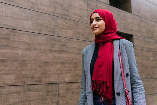 Content young Arab female wearing traditional hijab and casual clothes walking along city street and looking forward