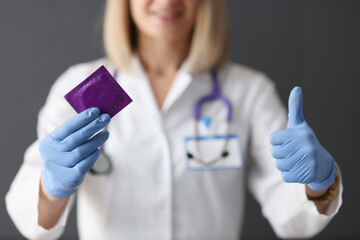 Doctor holding condom in his hands and showing thumb up closeup