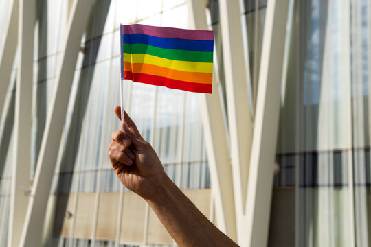 Low angle of cropped unrecognizable homosexual male standing on street with paper LGBT flags