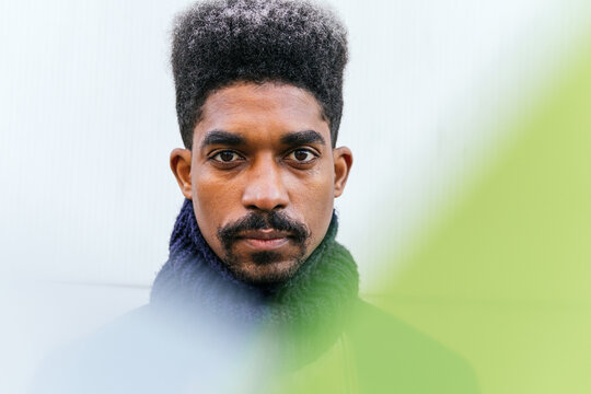 Through yellow light filter of carefree African American male with curly hair standing in white wall looking at camera