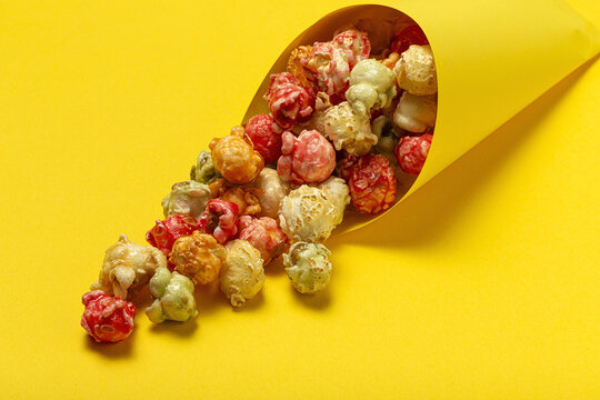 High angle of colorful tasty popcorn in paper cone placed on yellow background in studio