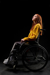 Fototapeta na wymiar hopeless female sits on wheelchair unhappy, with depressed expression on face, she is suffering from disability. isolated black background. side view