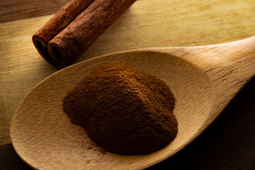 Colher de madeira com pó de canela e pedaço de canela sobre uma tábua de madeira.