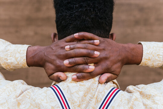 Back view of crop unrecognizable African American male in casual shirt keeping intertwined fingers on neck while relaxing and dreaming