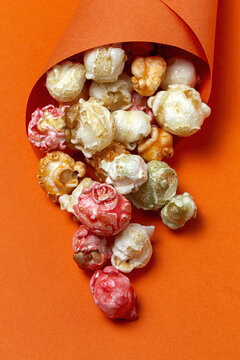 High angle of colorful tasty popcorn in paper cone placed on orange background in studio