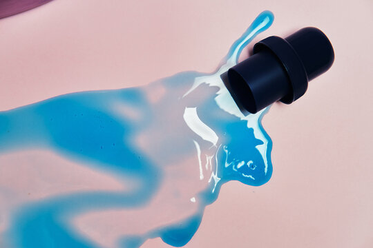 Top view of liquid detergent spilled from plastic cap on pink background in studio