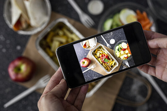 From above of crop unrecognizable blogger taking picture of takeaway food prepared for lunch while using smartphone