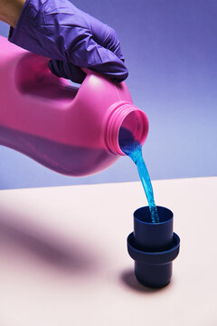 Crop anonymous person with plastic bottle pouring liquid detergent in cap placed on table in studio
