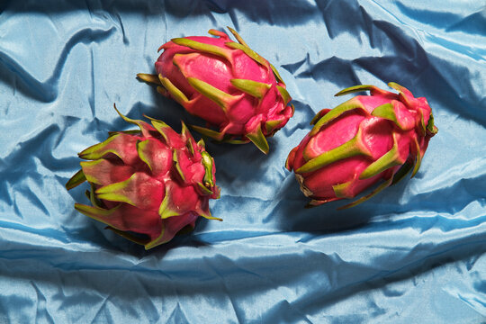 From above of whole fresh pitaya fruits arranged on blue wrinkled cloth in studio