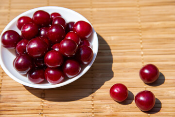 Dark red cherries in a white plate on a bamboo tablecloth. The concept of healthy berries and fruits.