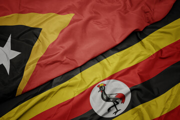 waving colorful flag of uganda and national flag of east timor.