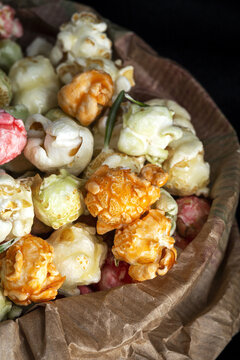 Heap of varicolored sweet popcorn in paper bag placed with yellow corn seeds on black background in studio