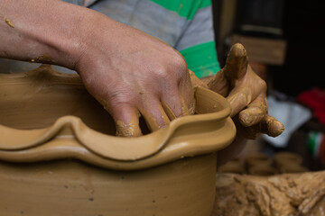 Wet and muddy hands of a craftsman shaping a clay vase on a pottery wheel. Artisan from Ráquira,...