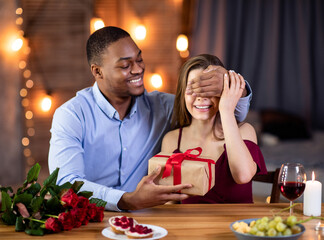 Loving Man Covering Girlfriend's Eyes And Presenting Gift At Date In Restaurant