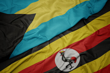 waving colorful flag of uganda and national flag of bahamas.