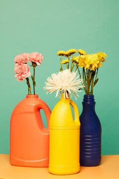 Various blooming flowers placed in colorful plastic bottles from detergents showing concept of reusable containers