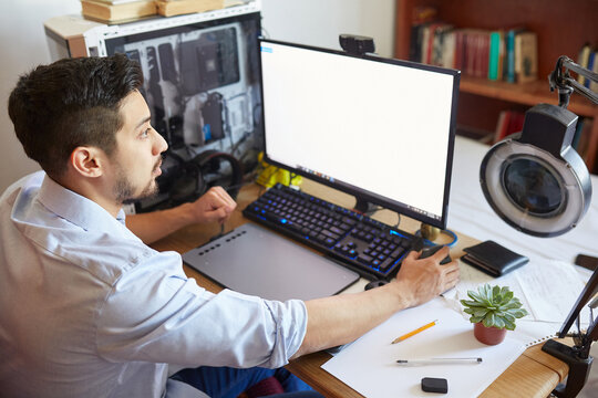 High angle side view of young male student sitting at table and working on computer monitor while preparing for exam in university