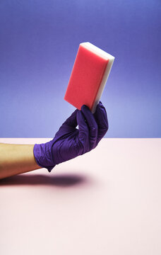 Unrecognizable crop person in glove demonstrating soft dishwashing sponge on purple background in studio