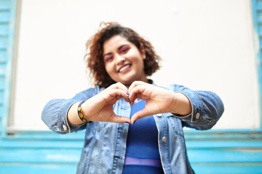 Low angle of plump cheerful female showing love sign while standing on street and looking at camera