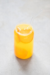 Fruit drink refreshing tangerine in a glass jar with a straw on a light gray background