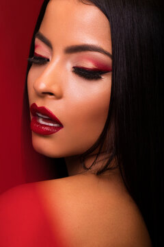 Magnificent female with red lips and in black dress standing with opened mouth and closed eyes on red background in studio