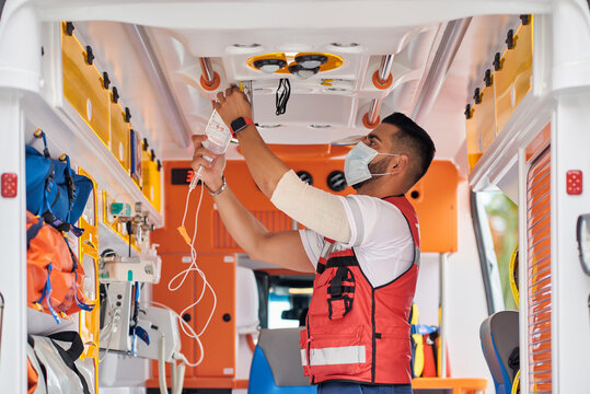 Side view of serious male paramedic in medical mask standing with dropper in modern ambulance van