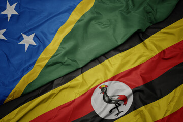 waving colorful flag of uganda and national flag of Solomon Islands .