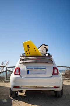 Modern white cabriolet automobile with surfboards parked on beach on sunny day in summer