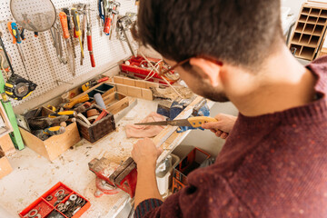 Side view high angle of busy male woodworker using sharp saw and cutting wooden plank in workshop
