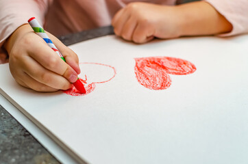 A little girl is drawing a heart with red chalk - high angle image with selective focus. Valentine's day concept