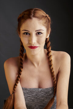 Stylish female model with red hair and braids sitting in studio on dark background and looking at camera