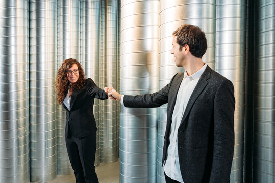 Delighted male and female coworkers in formal wear standing in storehouse and bumping fists while looking at each other and smiling