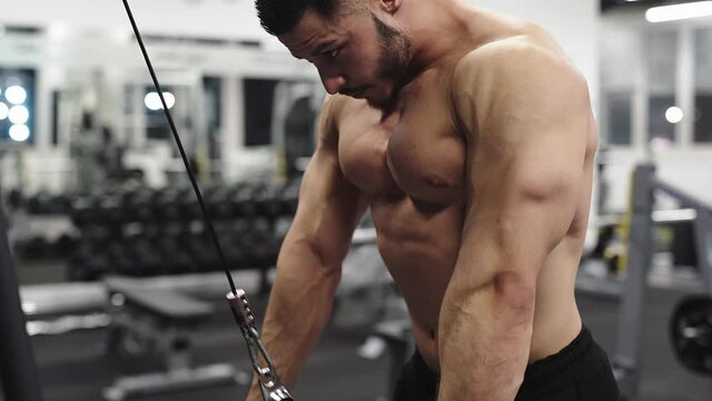 Topless muscular male sportsman doing bodybuilding triceps extensions in a crossover machine