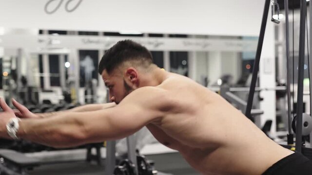Topless muscular male sportsman doing bodybuilding triceps extensions in a crossover machine