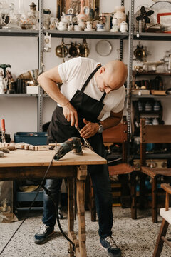 Focused middle aged carpenter using hammer and chisel while making wooden detail at table with professional tools in workshop