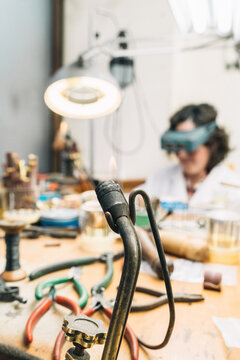 Metal soldering iron with flame used for jewelry work in professional workshop with female master working in background
