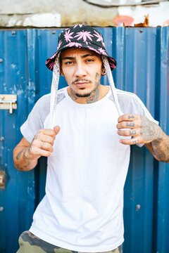 Young tattooed male hipster in informal clothing standing near metal fence and looking at camera